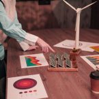 Cropped picture of engineers at office working on renewable ener Close up of ecology experts working on research of renewable energy with solar panels and wind turbine model on table. There are charts and graphs with diagrams and analysis related to ecology.